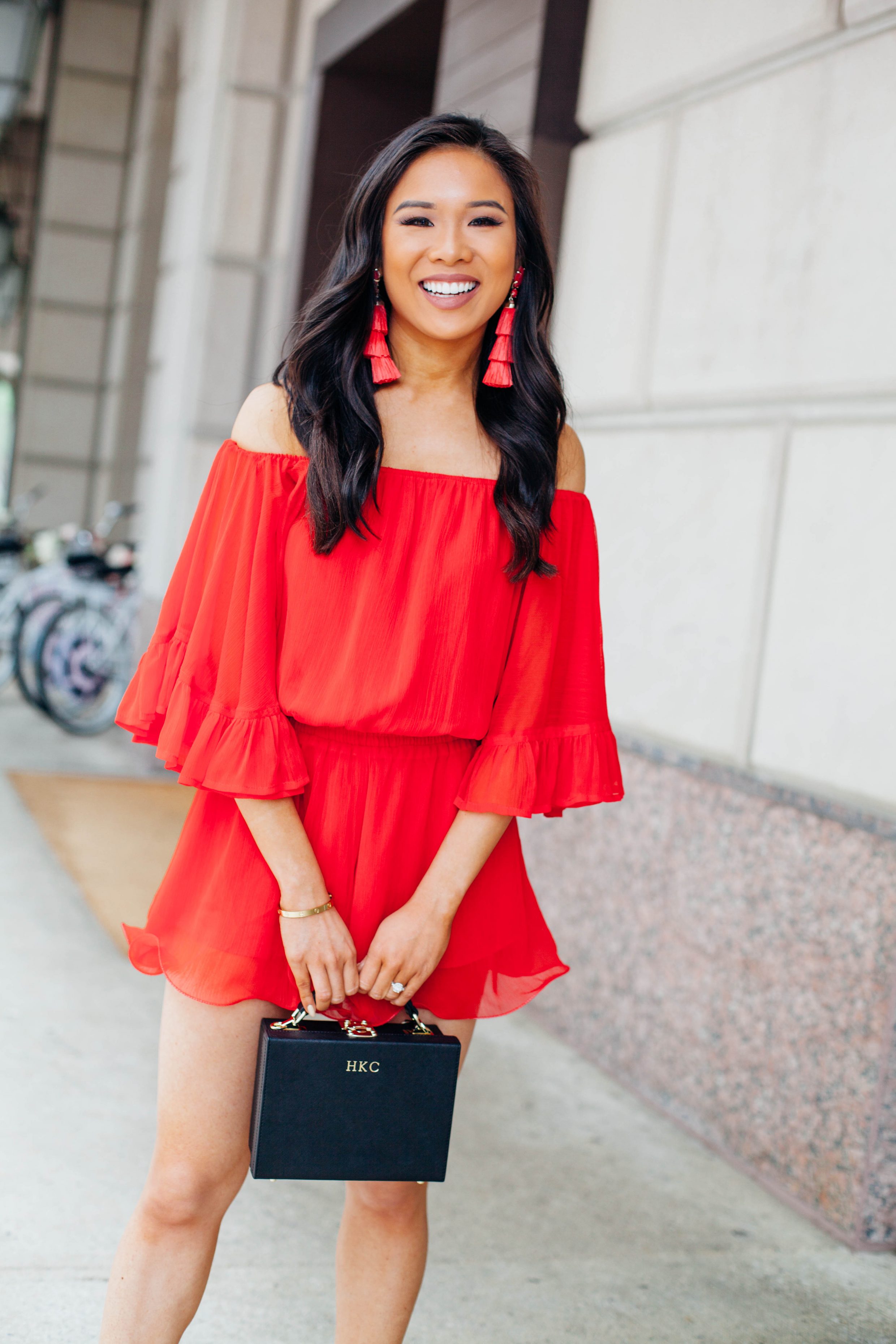 Hoang-Kim wears a red off the shoulder romper with tassel earrings and black box bag