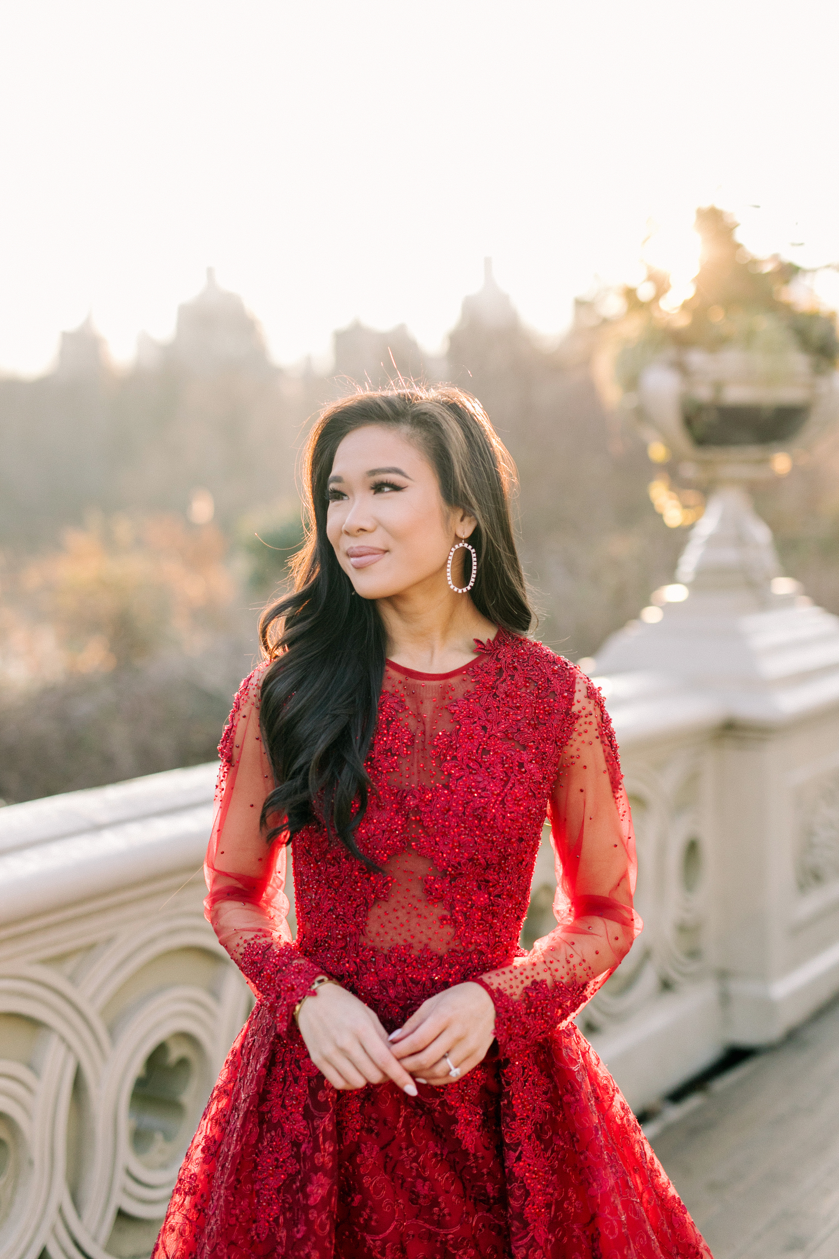 Hoang-Kim Cung wearing a MacDuggal long sleeve illusion lace ballgown, James Allen cushion diamond engagement ring and Kendra Scott Danielle open frame earrings for Central Park engagement photos