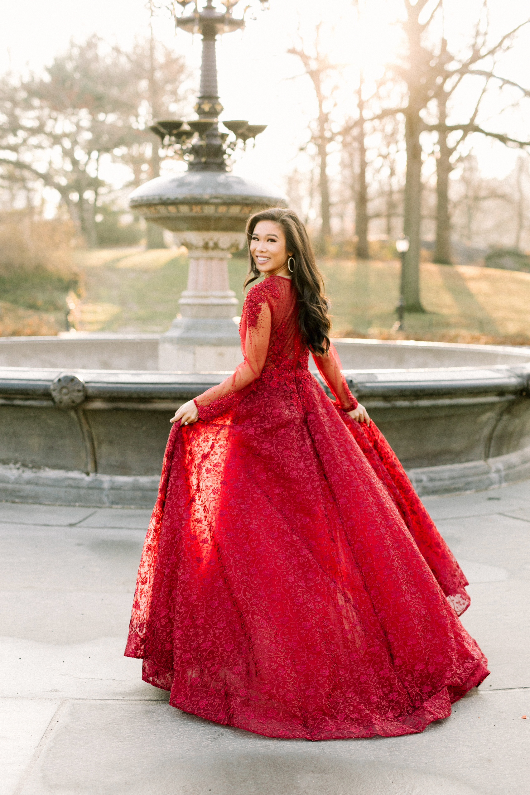 Hoang-Kim Cung wearing a MacDuggal long sleeve illusion gown in red and Kendra Scott Danielle open frame crystal earrings in Central Park for engagement photos