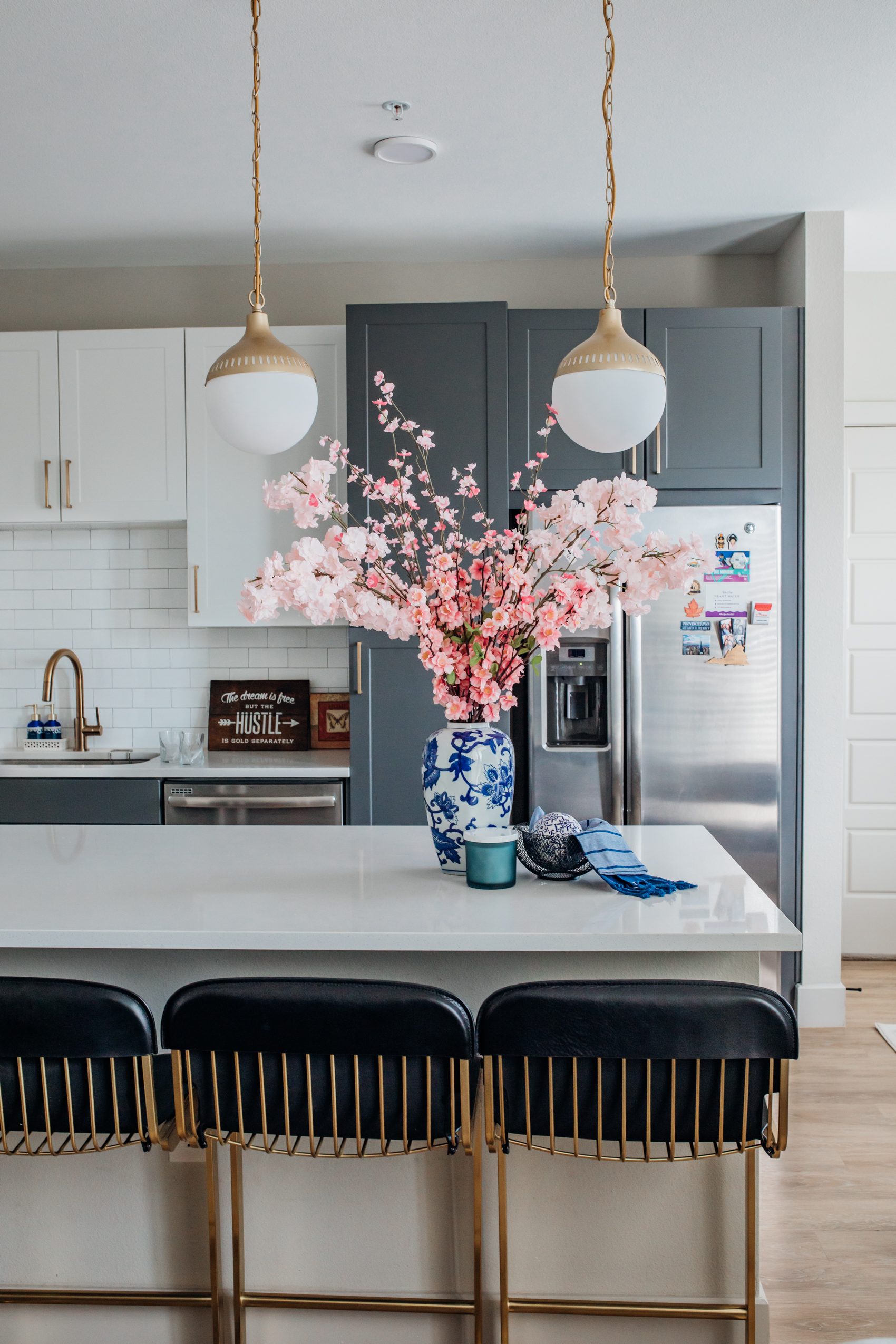 Two-toned kitchen with cherry blossoms, ginger gar, black leather barstools with gold legs, gold pendants and a gold sink faucet with subway tile