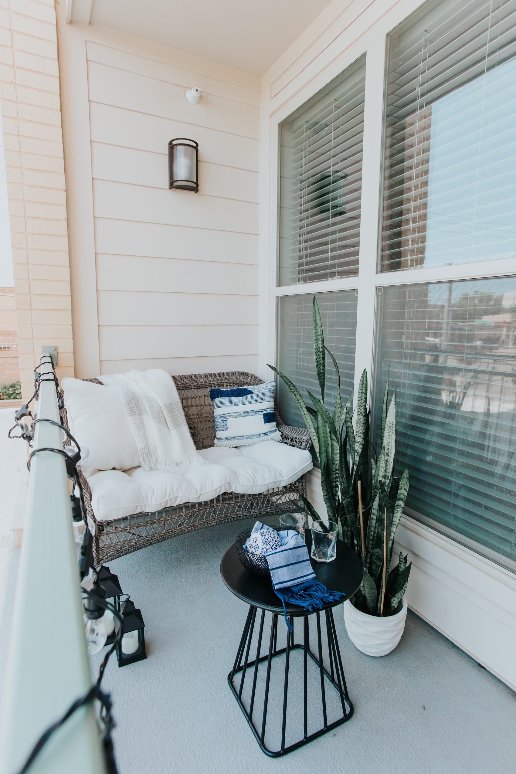 Apartment patio ideas with a gray wicker sofa, metal coffee table, snake plant, throw pillows and more on a budget
