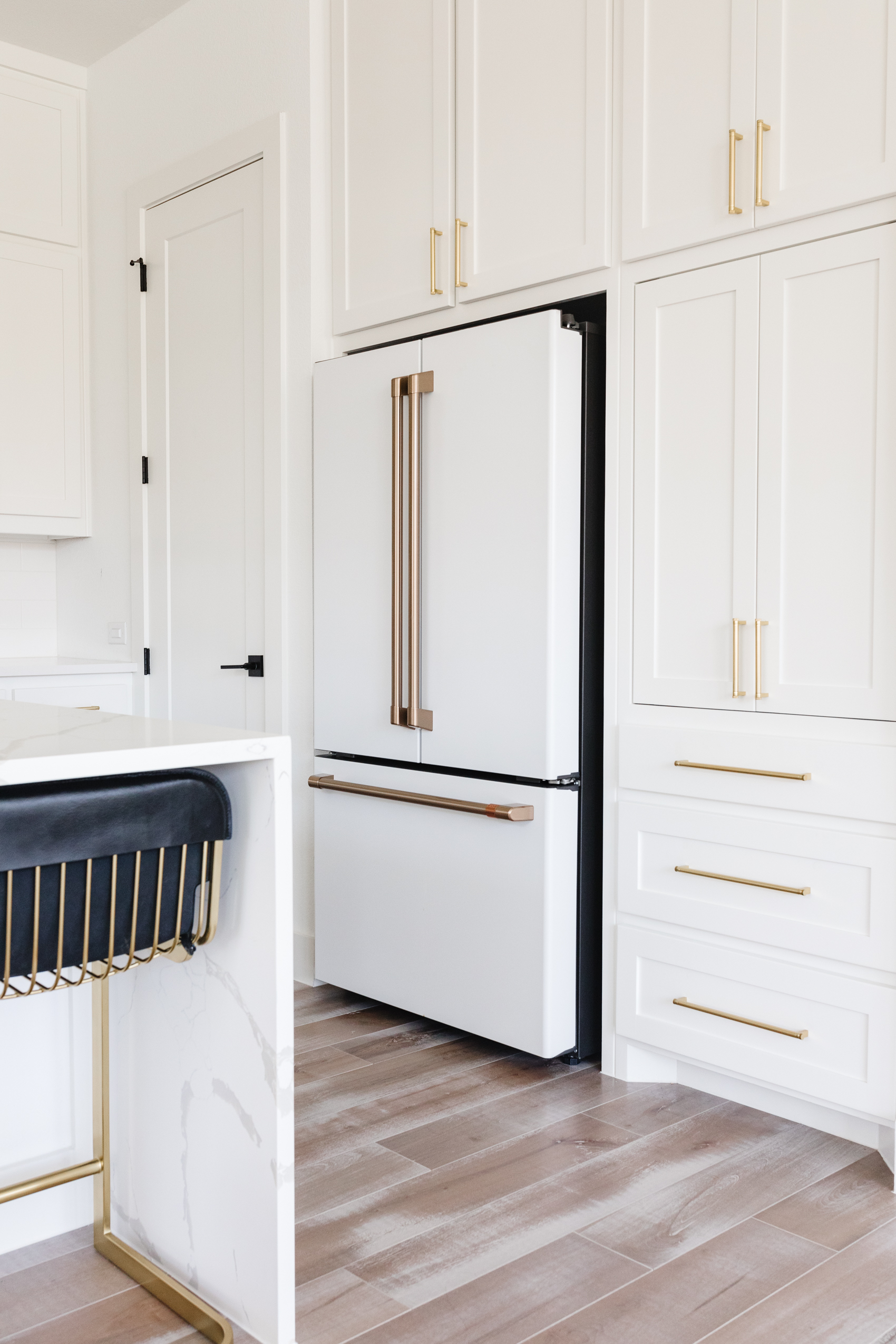 Cafe Appliances refrigerator in matte white with brushed bronze handles in a white kitchen with shaker style cabinets and brass hardware