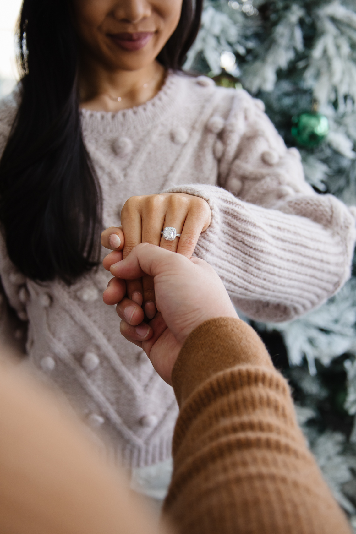 Asian couple with a James Allen cushion cut engagement ring in front of a flocked Christmas tree