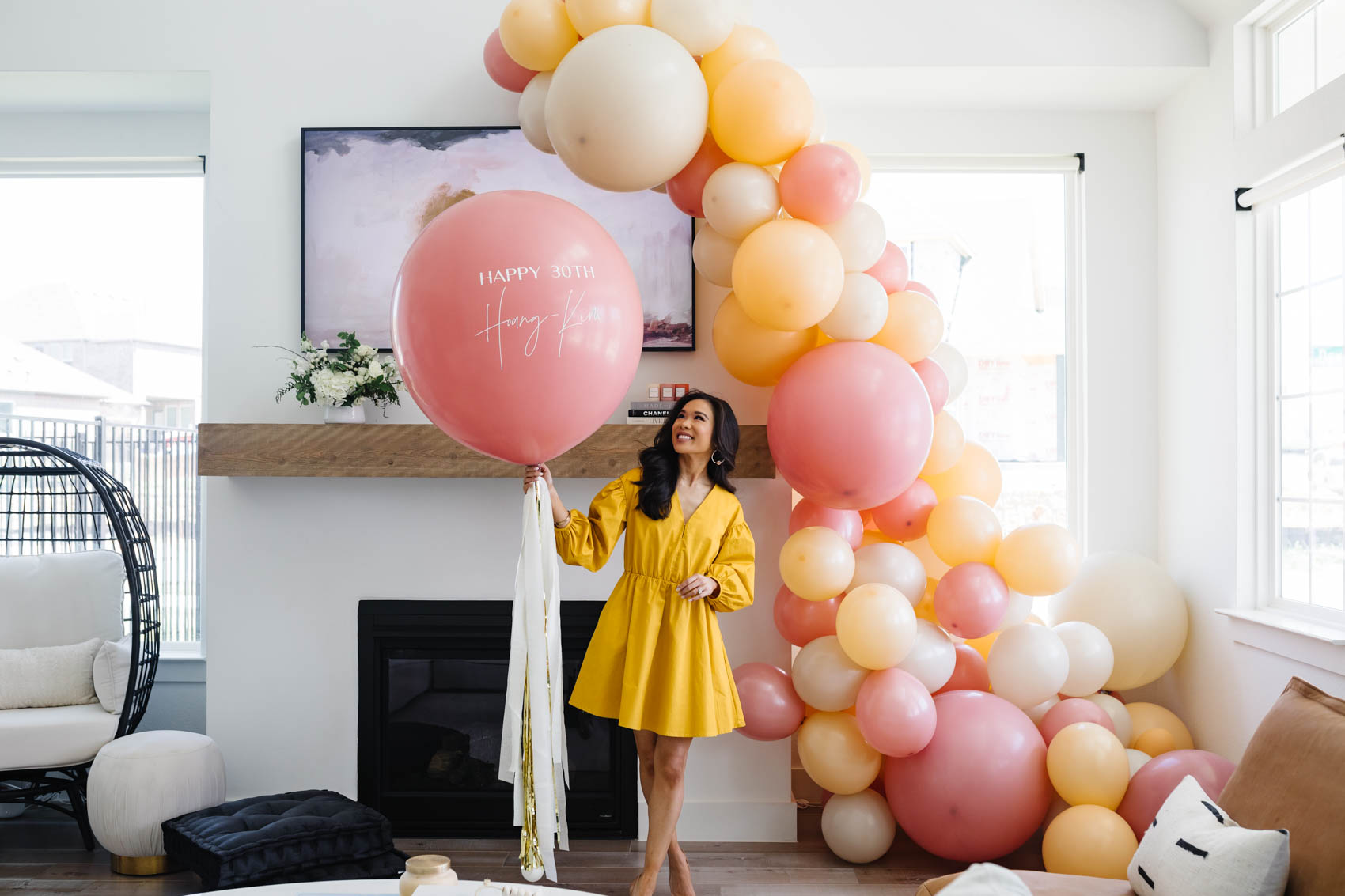 Hoang-Kim wears a yellow dress holding her custom jumbo balloon next to her organic balloon garland from Lushra